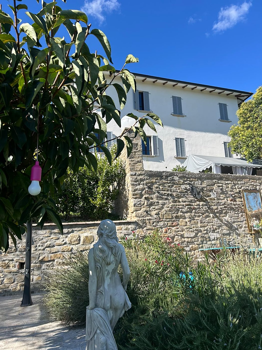 Een stenen vrouwenstandbeeld in de tuin, van achteren gezien, met het landhuis op de achtergrond