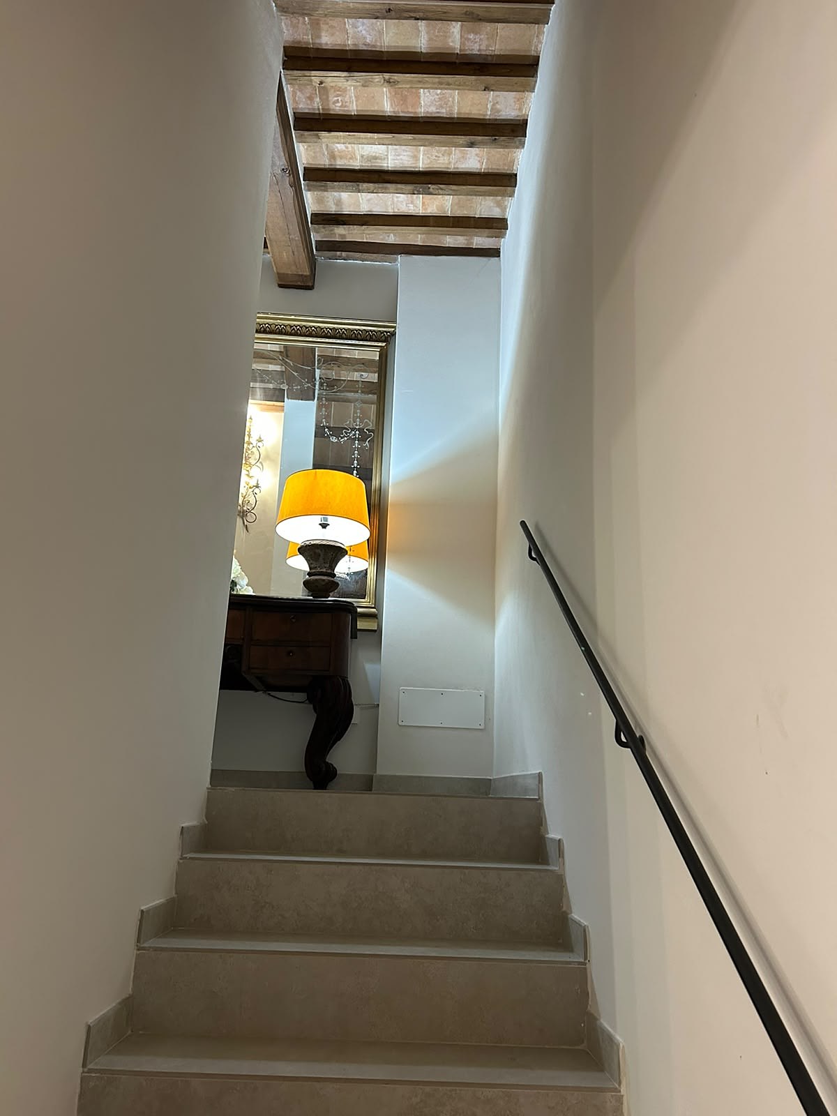 Omhoog kijkend vanaf de trap naar een vergulde spiegel en een lamp met een gele kap op een houten kastje
