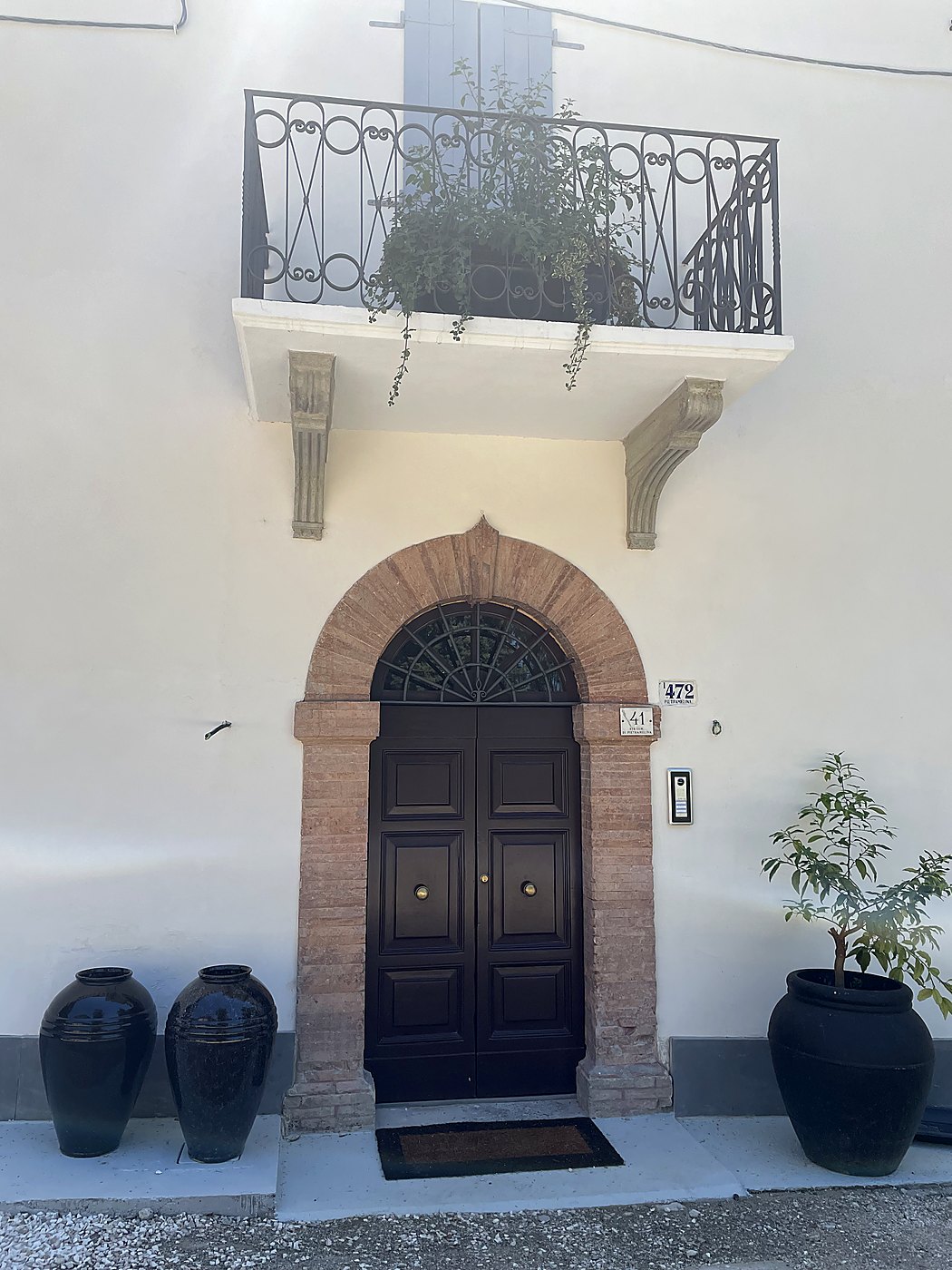 De voordeur van Casa Tira Mi Su in een bakstenen boog, met een balkon en grote zwarte potten